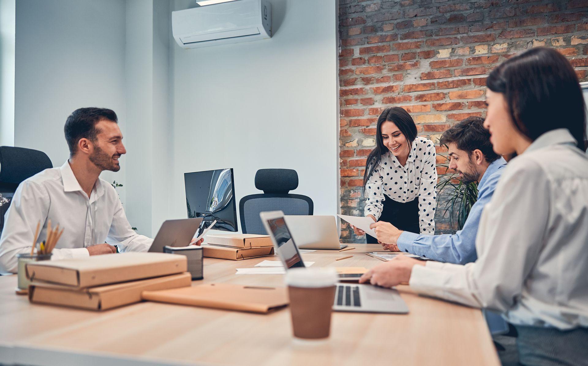 Group of people in an office meeting around a table with laptops and documents.